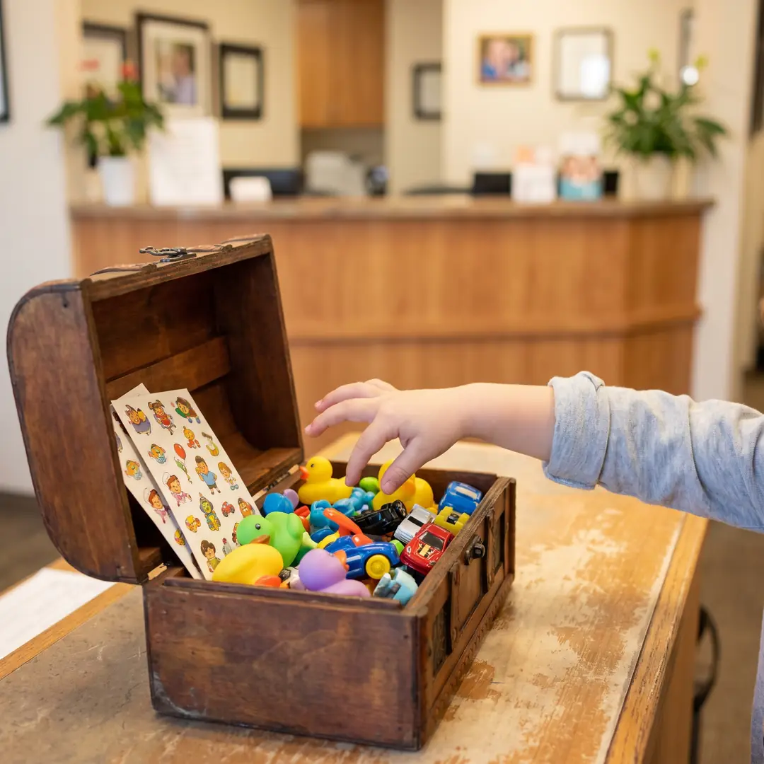 An open wooden treasure chest by the front desk, filled with small toys, stickers and bouncy balls for children to choose from after a visit